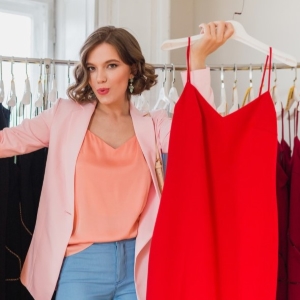 A lady holds a red dress triumphantly having chosen to sell it because she never wears it.